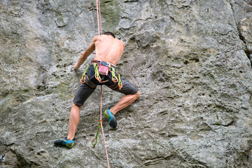 Strong male climber climbing steep wall of rocky mountain. Sportsman overcoming difficult route. Engaging in extreme sports hobby concept