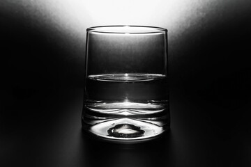 Transparent glass with water half full on black background and spot of light from above