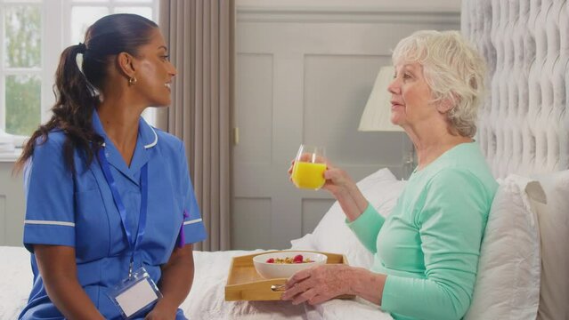 Female care worker in uniform bringing breakfast on tray to senior woman in bed  at home - shot in slow motion