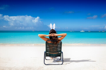 A woman with easter bunny ears relaxes on a sunchair at a tropical paradise beach