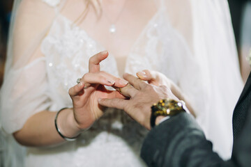 Bride puts a wedding gold ring on groom's finger in church during the wedding ceremony