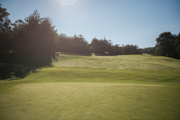 Golf course landscape with short green grass, some hills and trees.
