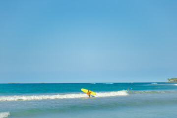 Blue sea waves under a blue sky near a tropical beach. Yellow surf on a white wave. Summer sunny morning off the coast of the Atlantic. Outdoor activities.