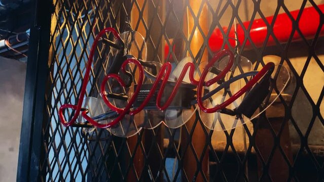 Red neon love sign flickering out with a metal fence and pipes in the background