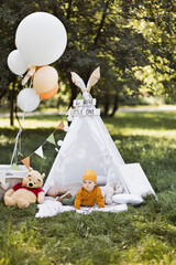 Cute caucasian baby boy in stylish clothes playing in colorful wigwam among summer nature. Concept of childhood, picnic and family time. © Sofiia Shunkina