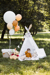 Adorable caucasian boy sitting in colorful wigwam among green nature. Cute child with balloons and toys playing outdoors. Funny time spending. © Sofiia Shunkina