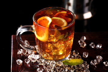 Black tea with ice cubes and mint on a black background