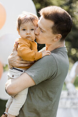 Young caring father kissing and embracing his little son while standing among green nature near...