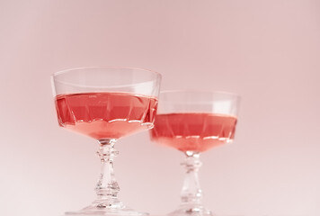 Two crystal glasses of rose sparkling wine or champagne on pastel pink background. Summer drink concept. Minimal creative composition with copy space.
