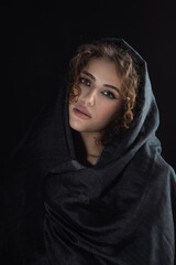 beautiful young woman with dark grey headscarf cover her face with luxury makeup on black background looking down