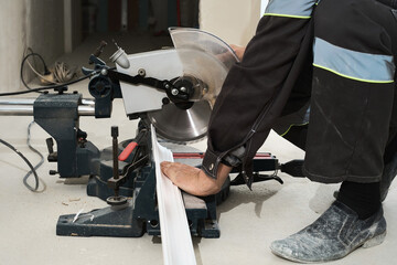 Construction worker uses a portable circular saw to cut a styrofoam baseboard. Circular saw with a sharp rotating blade, new baseboard, woodworking machinery, equipment