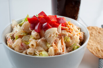 Tuna salad in a white bowl with lettuce pasta mayo carrots and red peppers on top with a dark soft...