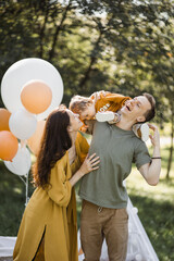 Happy caring mother embracing and kissing her little son that sitting on strong father's shoulders. Caucasian family spending summer time on fresh air with fun and relaxation. © sofiko14