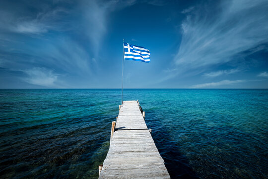 Greek flag on a beautiful sunny day at the end of a white wooden pier. Corfu Greece