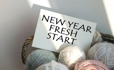 A card with the inscription NEW YEAR NEW START in a basket with balls of thread. Delicate colors, light background. Congratulations and wishes. Beginning of the year, beginning of spring.