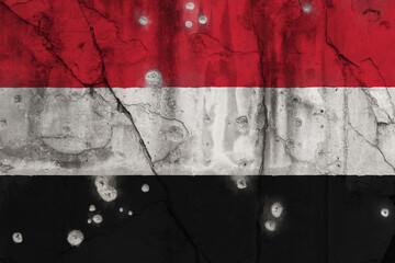 Full frame photo of a weathered flag of Yemen painted on a cracked wall with bullet holes. Yemeni Crisis and civil war concept.