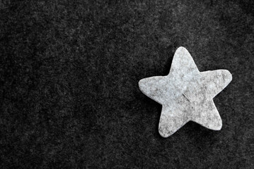 close-up of a cut-out pattern gray star made of felt on a dark gray background. copy space