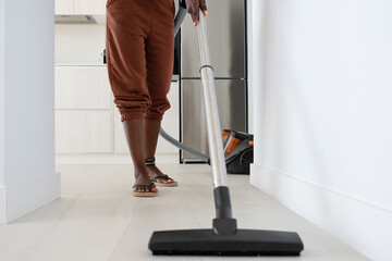 Crop female vacuuming floor in hallway