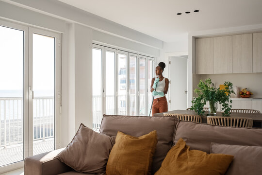 African housewife with mop looking out window