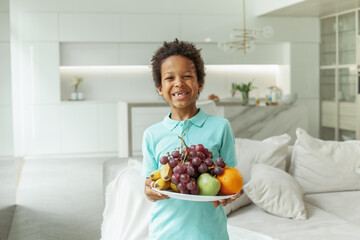 Kid boy with black hair and cute smile holding fruit indoor