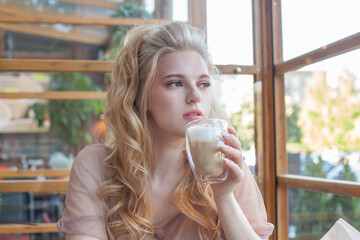 Beautiful blonde young woman drinking coffee at the cafe, looking away.
