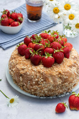 Homemade gingerbread cake garnished with fresh strawberries on a light gray background. Summer still life outdoors