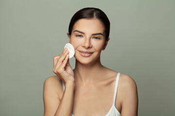 Young brunette woman removing makeup from her face with cotton pads. Skin care and beauty concept.