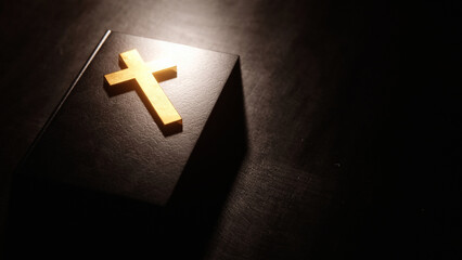 Golden Christian cross resting on Bible illuminated by light coming from above.