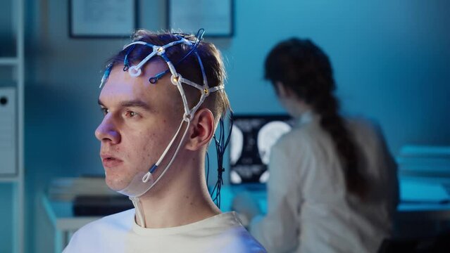 Man wearing EEG topographer for examining brain, doctor making electrogram of scalp activity. Researching of brain work using electroencephalography headset.