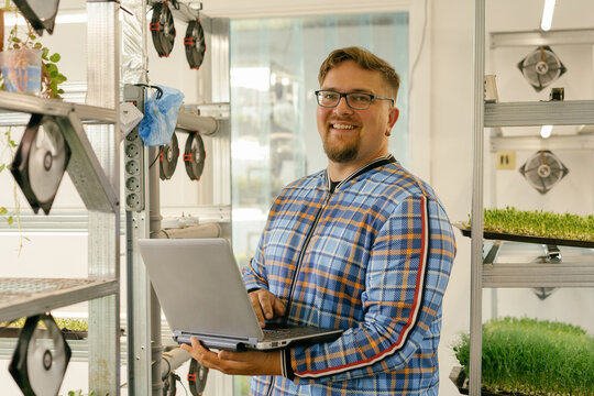 Man with laptop next to microgreen plantations