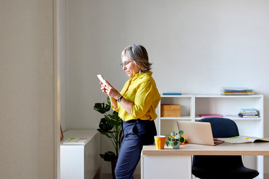 Stylish woman messaging on smartphone in office