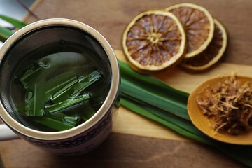 Uma caneca de chá de capim limão, uma colher de ervas, algumas rodelas de laranja desidratada sobre uma superfície de madeira.