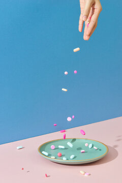 Hand and falling pills on pink table