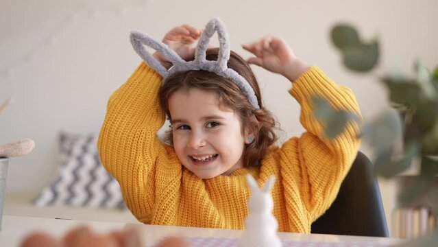 Portrait of funny girl with headband with ears looking at camera and reading. Preparation and celebration of Easter party.