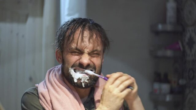 A man in the bathroom in front of the mirror furiously brushes his teeth with a toothbrush like crazy