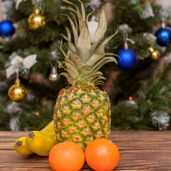 New Year and Christmas. Tropical fruits on a wooden table. Tangerines, bananas and pineapple on a wooden background opposite the Christmas tree.