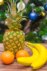 New Year and Christmas. Tropical fruits on a wooden table. Tangerines, bananas and pineapple on a wooden background opposite the Christmas tree.