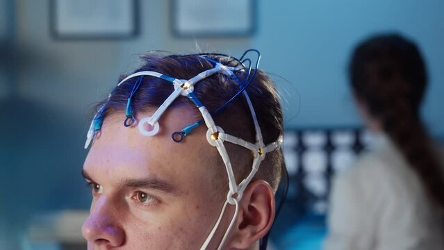 Man wearing EEG topographer for examining brain, doctor making electrogram of scalp activity. Researching of brain work using electroencephalography headset.