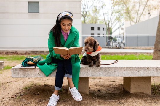 Asian woman reading with her doggy at park bench