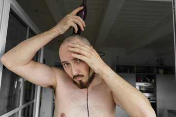 A serious guy shaving head at home