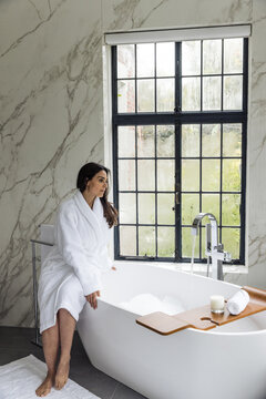 Woman sitting on the edge of tub in a bathrobe