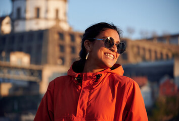 A portrait of a cheerful young woman from Spain in sunglasses and a vibrant jacket outdoors