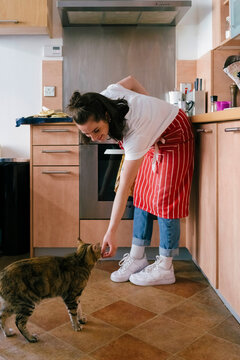 Woman feeding their cat while cooking