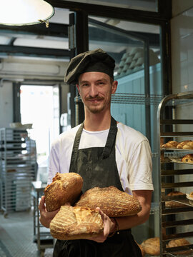 Artisan baker holding loafs of bread in the shop
