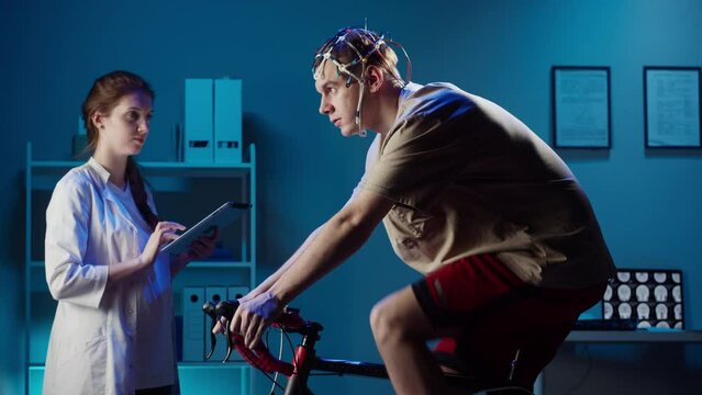 EEG topographer for examining brain, doctor making electrogram of scalp activity. Researching of brain work, man riding bicycle in electroencephalography headset. Rehabilitation after damage in sport.