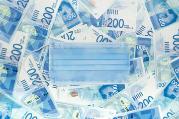 Concept of Israel Finance during covid epidemic. Medical Face mask on Heap of banknotes in nominal 200 New Israeli Shekels. Top view