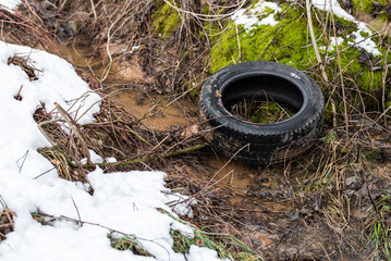 Random garbage junk items left in nature. Old tire in the ditch on winter day.