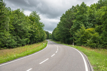 Deserted winding road through a forest under storm clouds in the countryside of Germany in summer