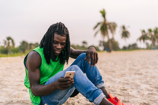 Black man browsing smartphone on beach