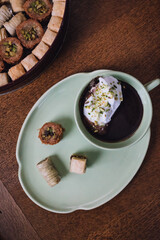 Fototapeta na wymiar drinking chocolate in matching green cup and plate with assorted baklava desserts on wood table